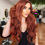 A woman with Trc long, wavy, coppery auburn hair is shown indoors, likely in a salon or styled interior, wearing a black top. The product appears to be the wig or hair color presentation rather than the room itself.